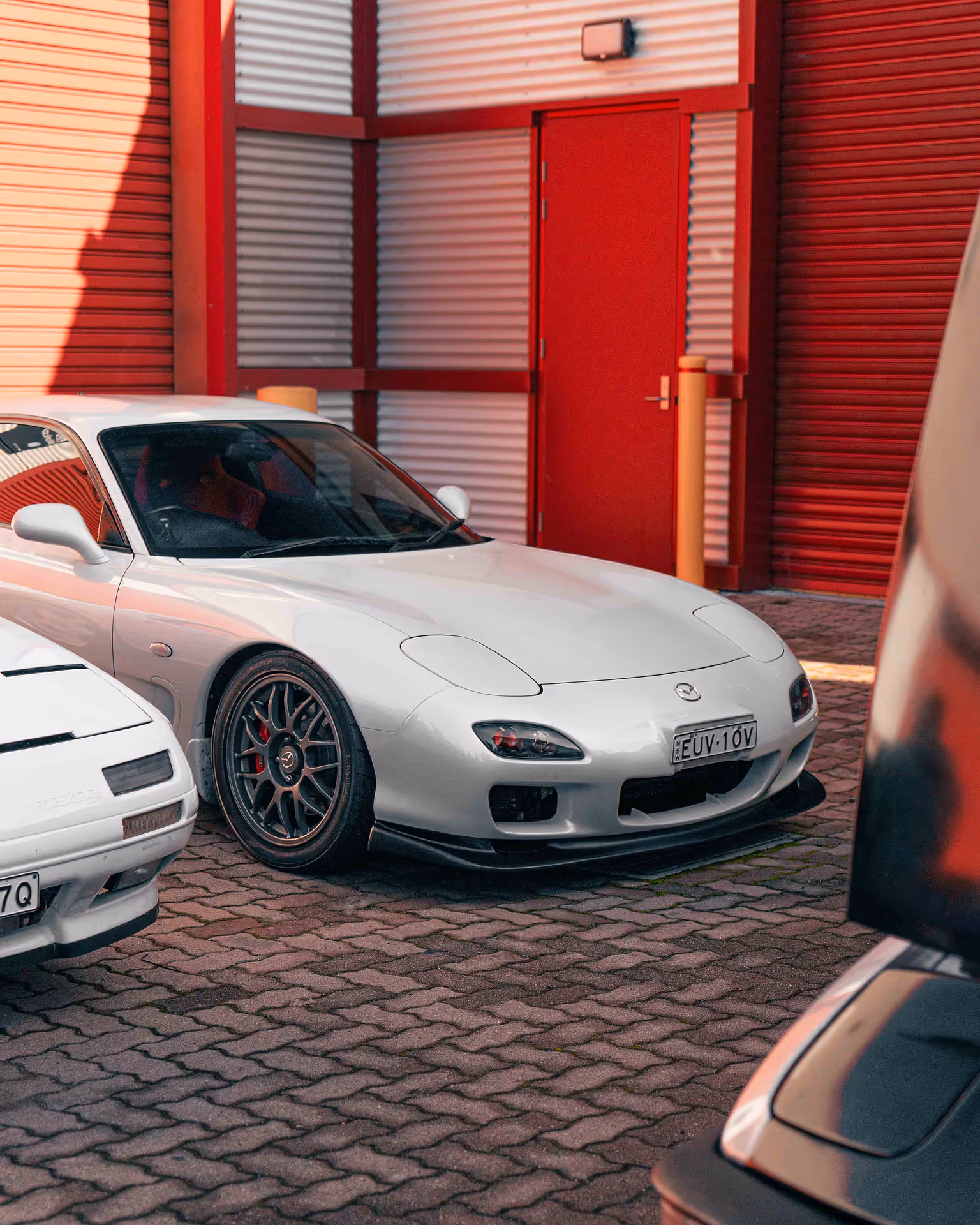 The front of a white car, with a red building in the background