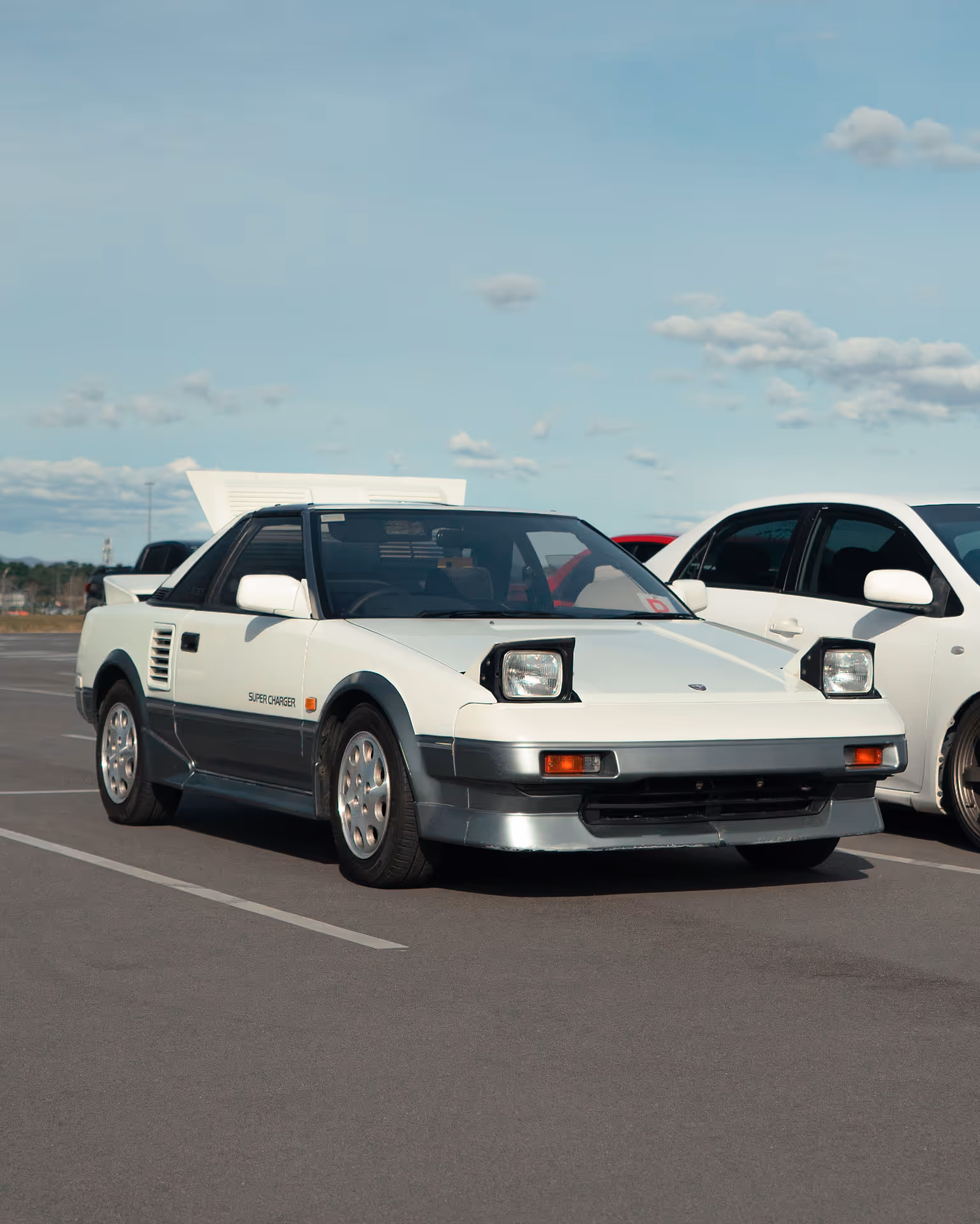 A white car with popup headlights and clear blue skies